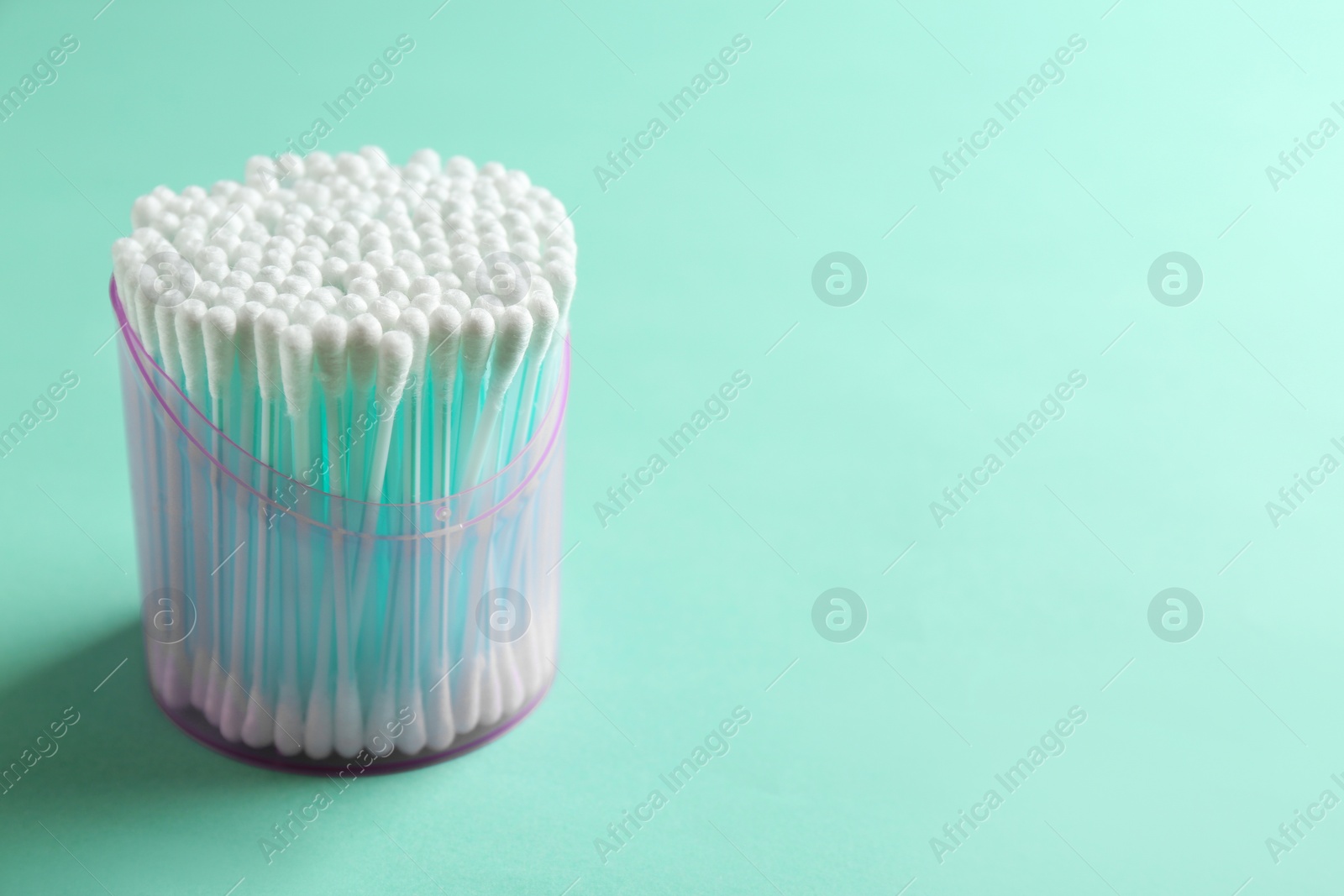 Photo of Plastic container with cotton swabs on color background. Space for text