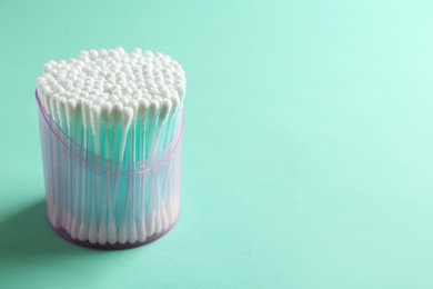 Photo of Plastic container with cotton swabs on color background. Space for text