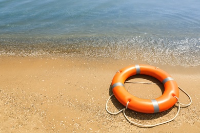 Photo of Orange life buoy on sand near sea. Emergency rescue equipment