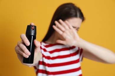 Young woman covering eyes with hand and using pepper spray on yellow background