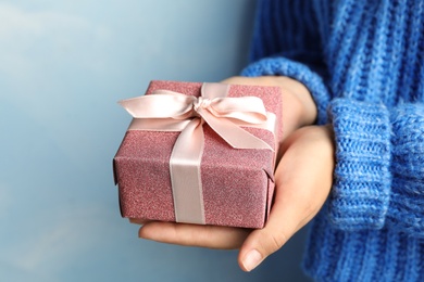 Young woman holding Christmas gift on blue background, closeup