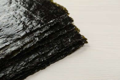 Photo of Stack of dry nori sheets on white wooden table, closeup. Space for text
