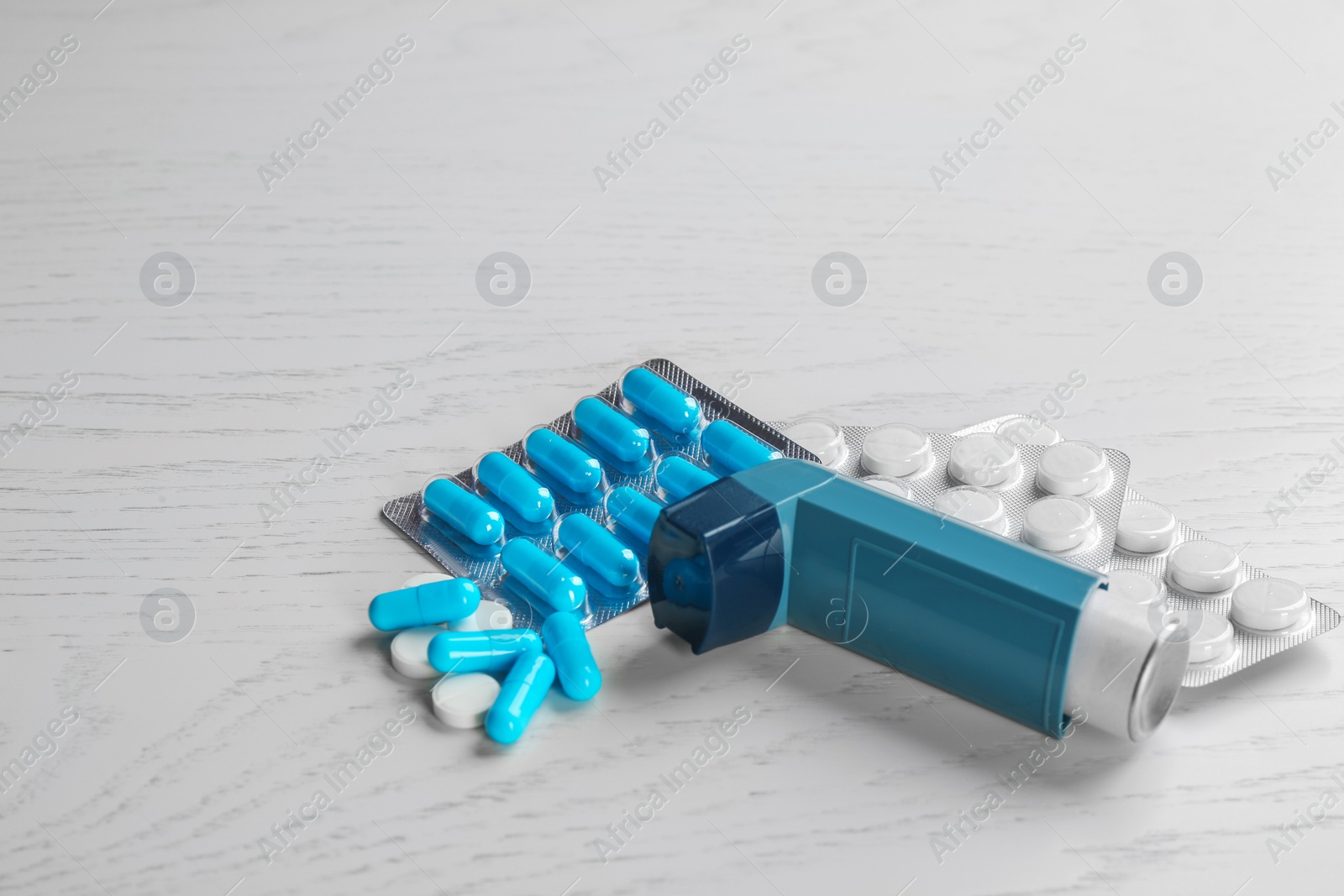 Photo of Asthma inhaler, pills and space for text on white wooden background