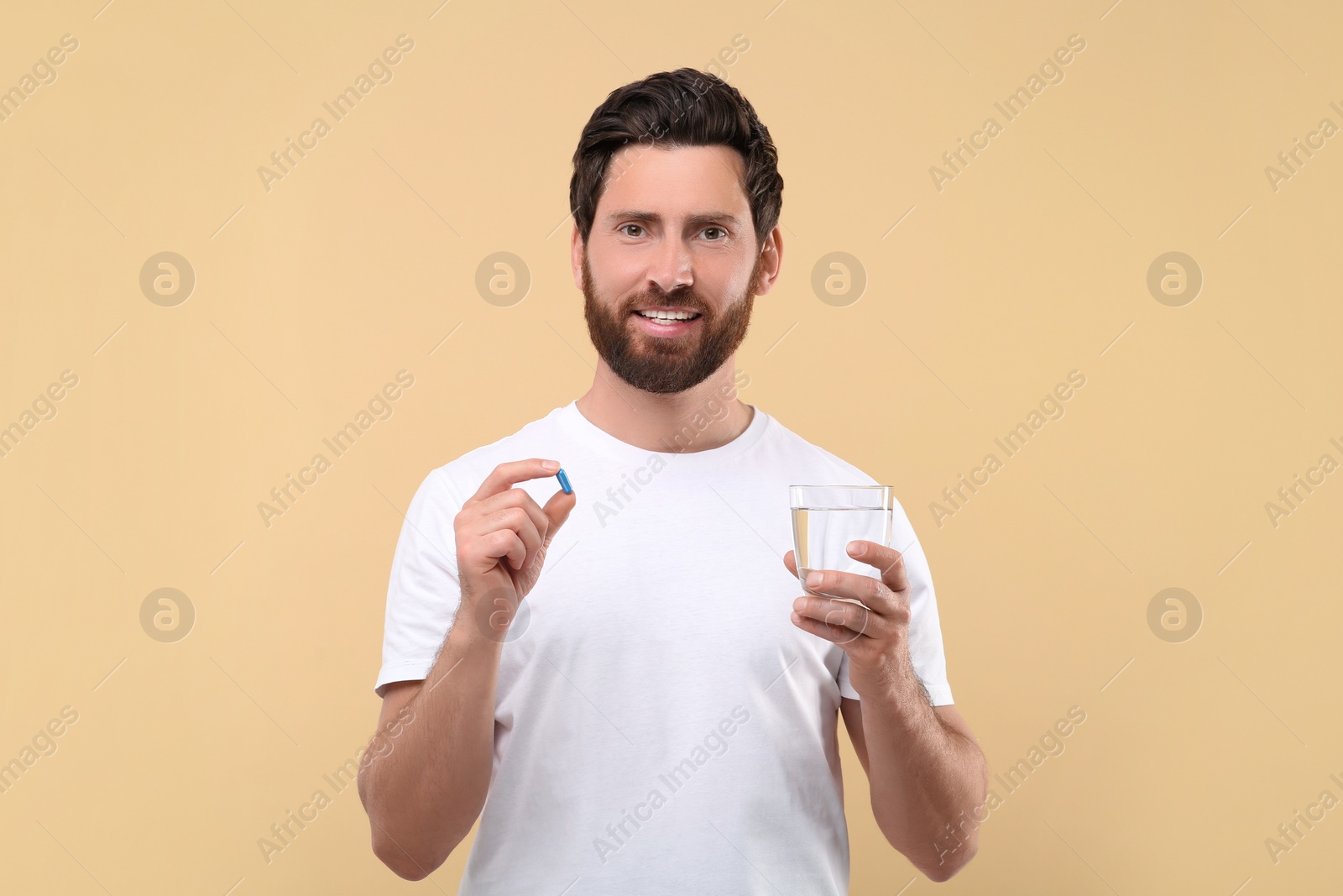 Photo of Handsome man with glass of water and pill on beige background