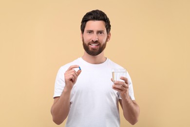 Photo of Handsome man with glass of water and pill on beige background