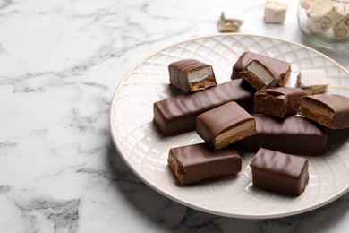 Photo of Tasty chocolate bars with nougat on white marble table, space for text