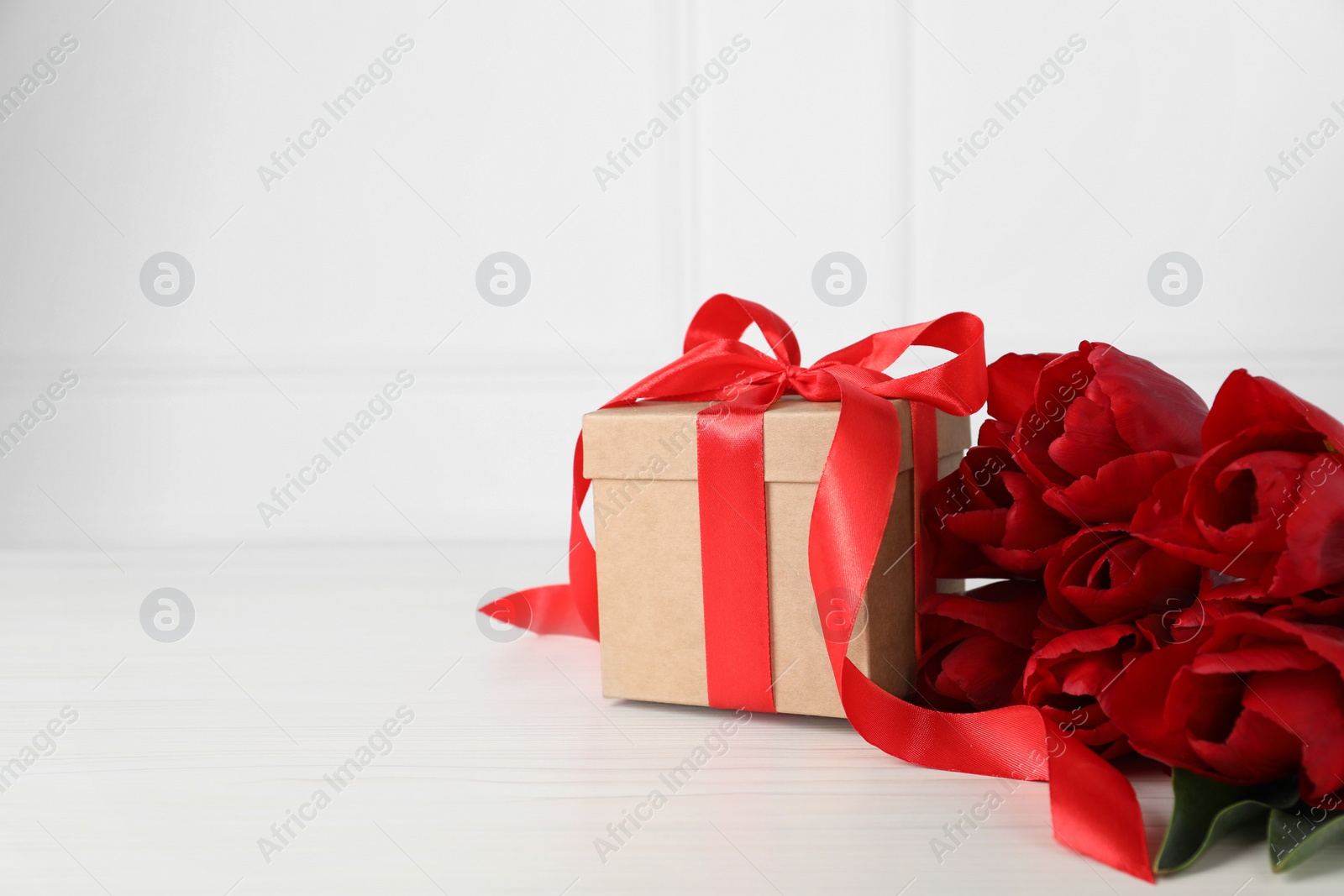 Photo of Beautiful gift box and red tulip flowers on white wooden table, space for text