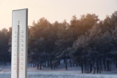 Thermometer showing temperature in snowy forest, winter weather