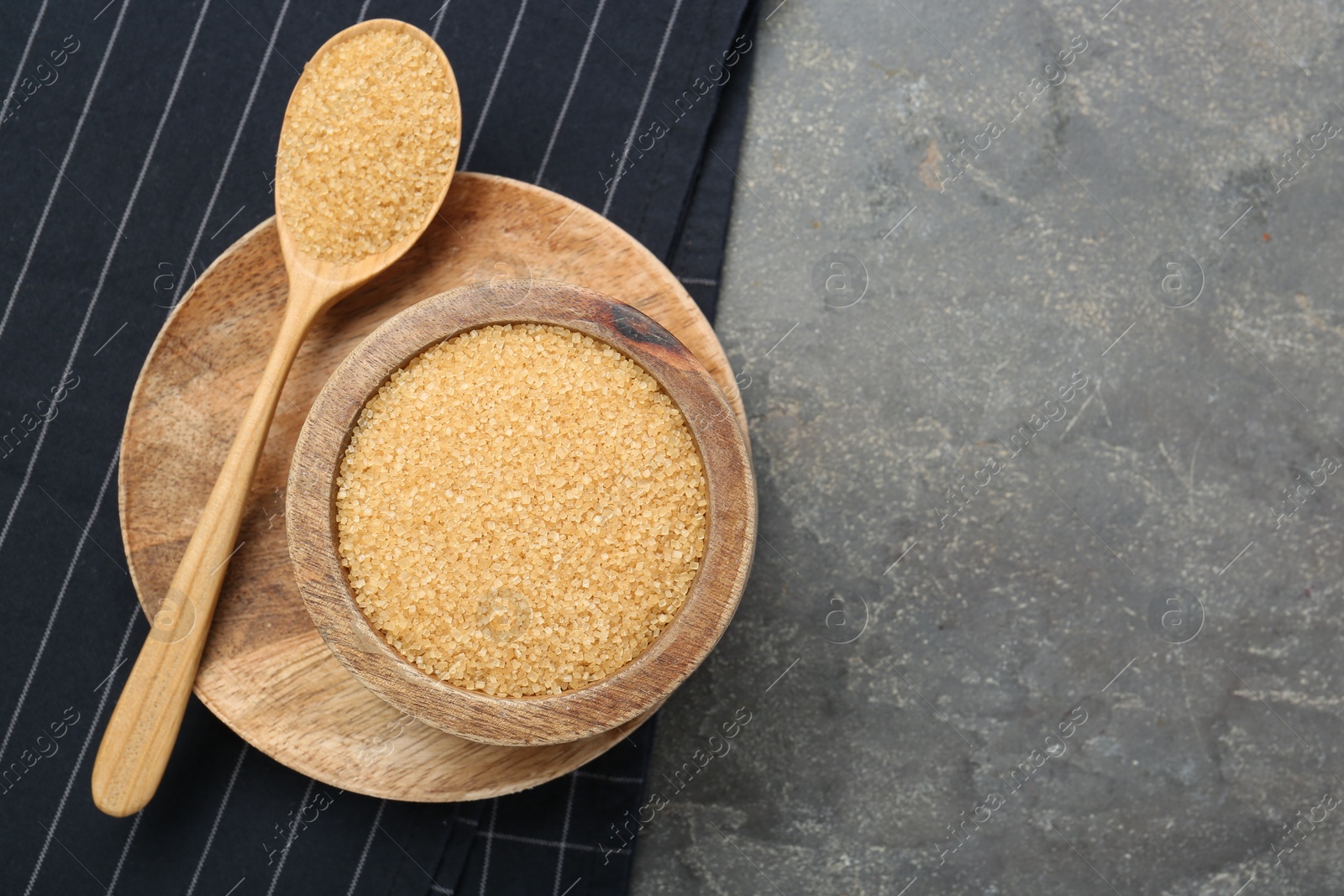 Photo of Brown sugar in bowl and spoon on grey textured table, top view. Space for text