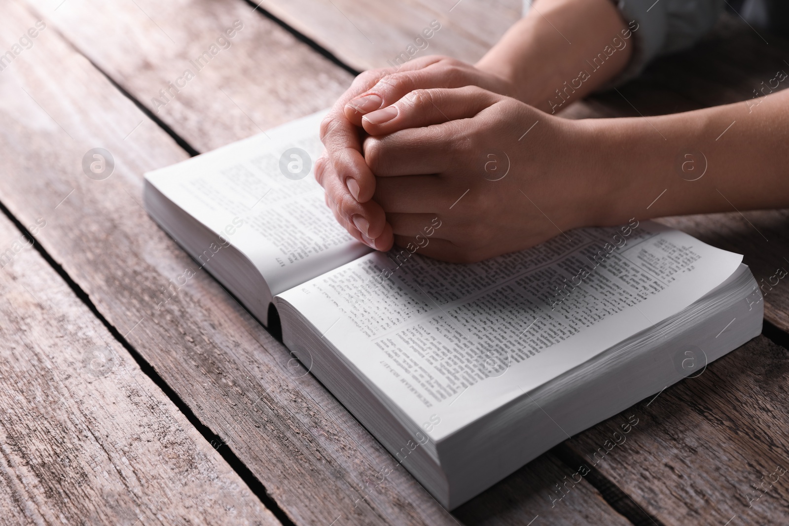 Photo of Religion. Christian woman praying over Bible at wooden table, closeup