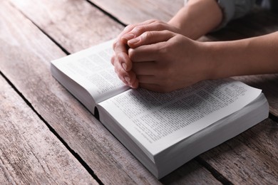 Photo of Religion. Christian woman praying over Bible at wooden table, closeup