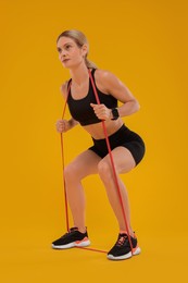 Photo of Woman exercising with elastic resistance band on orange background, low angle view