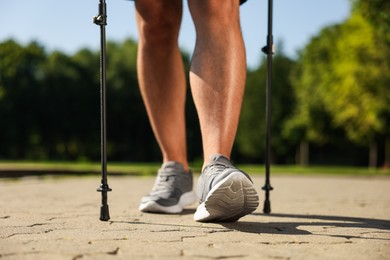 Photo of Man practicing Nordic walking with poles outdoors on sunny day, closeup