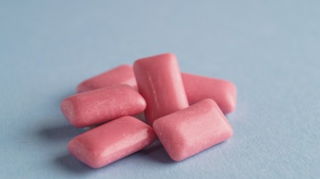 Photo of Heap of tasty sweet chewing gums on light blue background