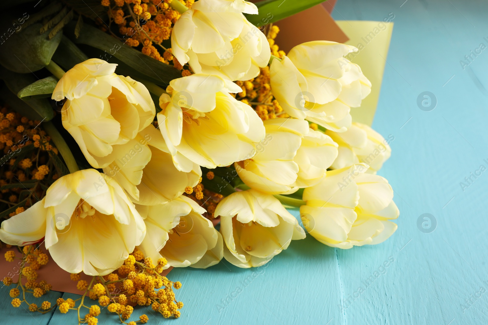 Photo of Bouquet with beautiful tulips and mimosa flowers on light blue wooden table