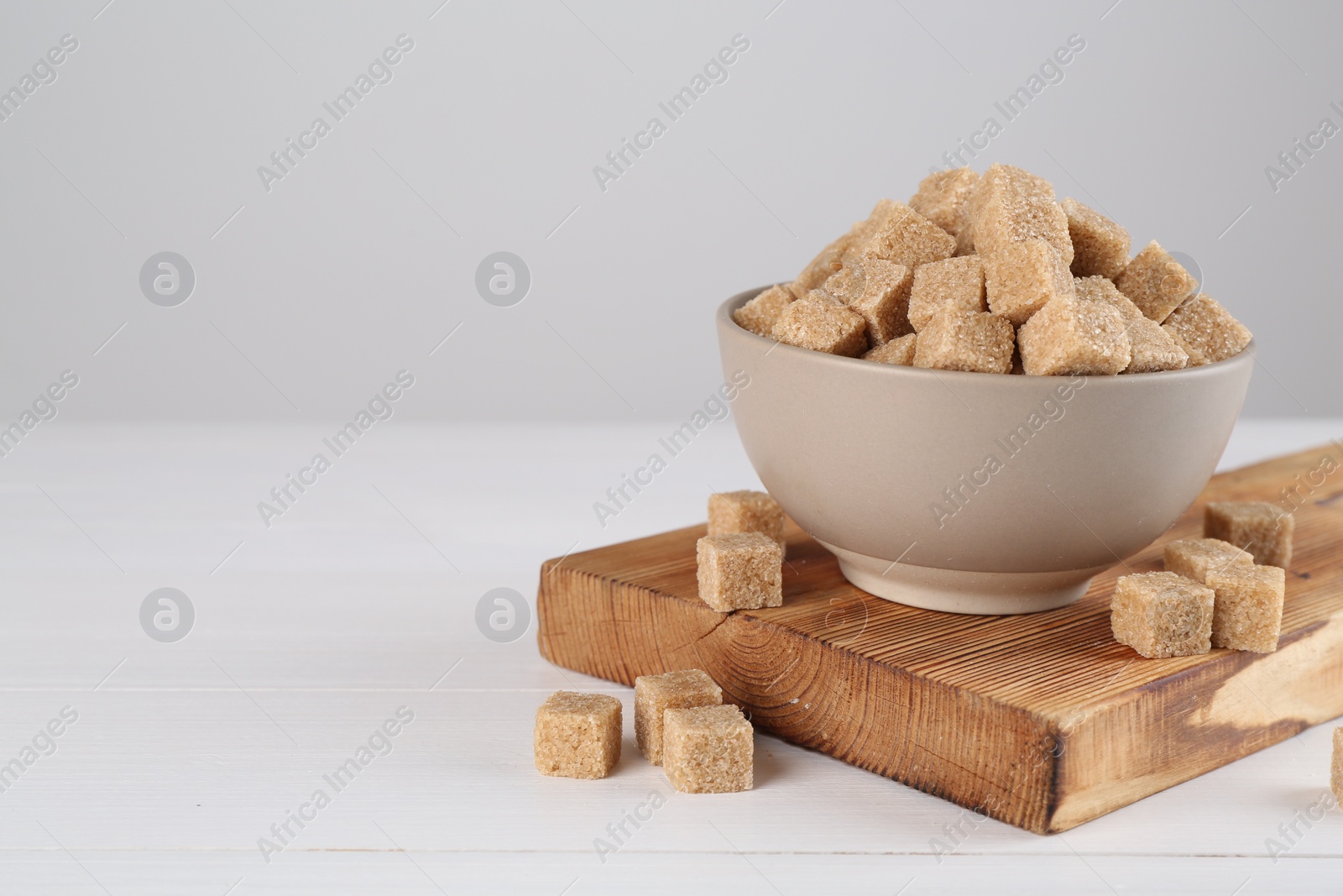 Photo of Brown sugar cubes on white wooden table, space for text