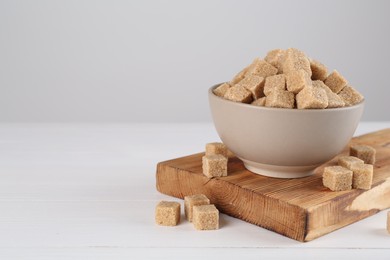 Photo of Brown sugar cubes on white wooden table, space for text