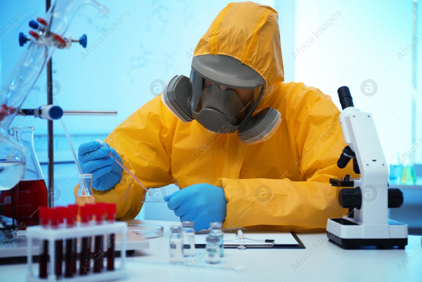 Photo of Scientist in chemical protective suit dripping reagent on microscope slide at laboratory. Virus research