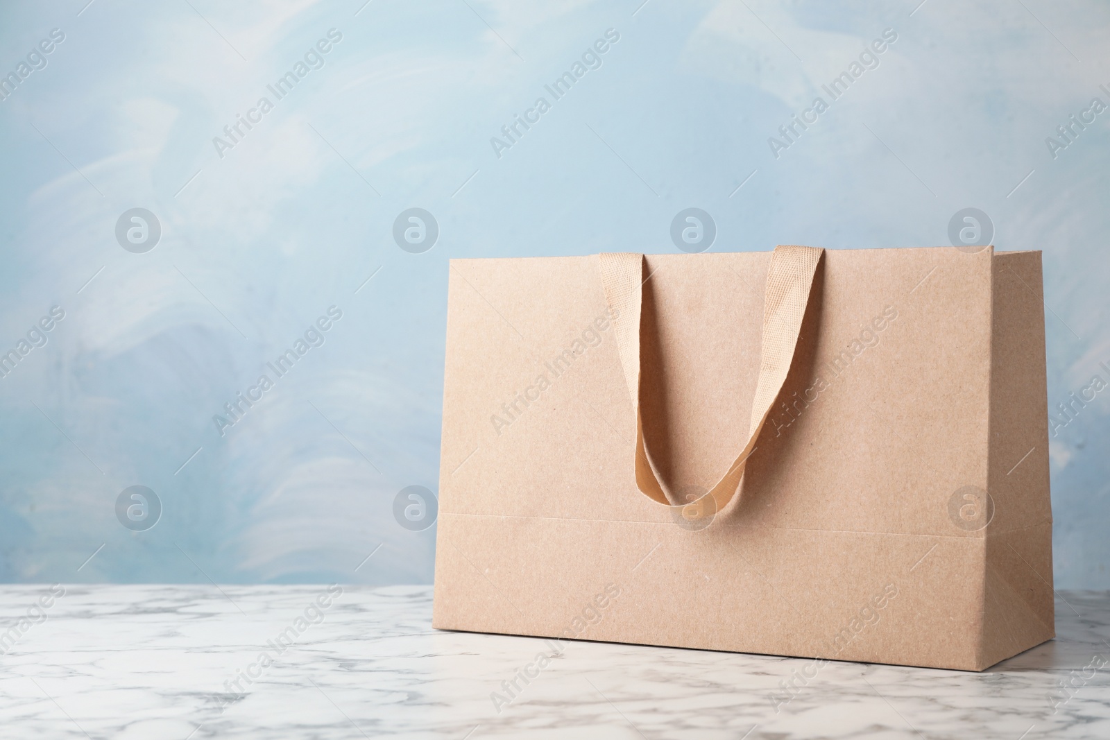 Photo of Paper shopping bag with comfortable handles on table against color background. Mockup for design