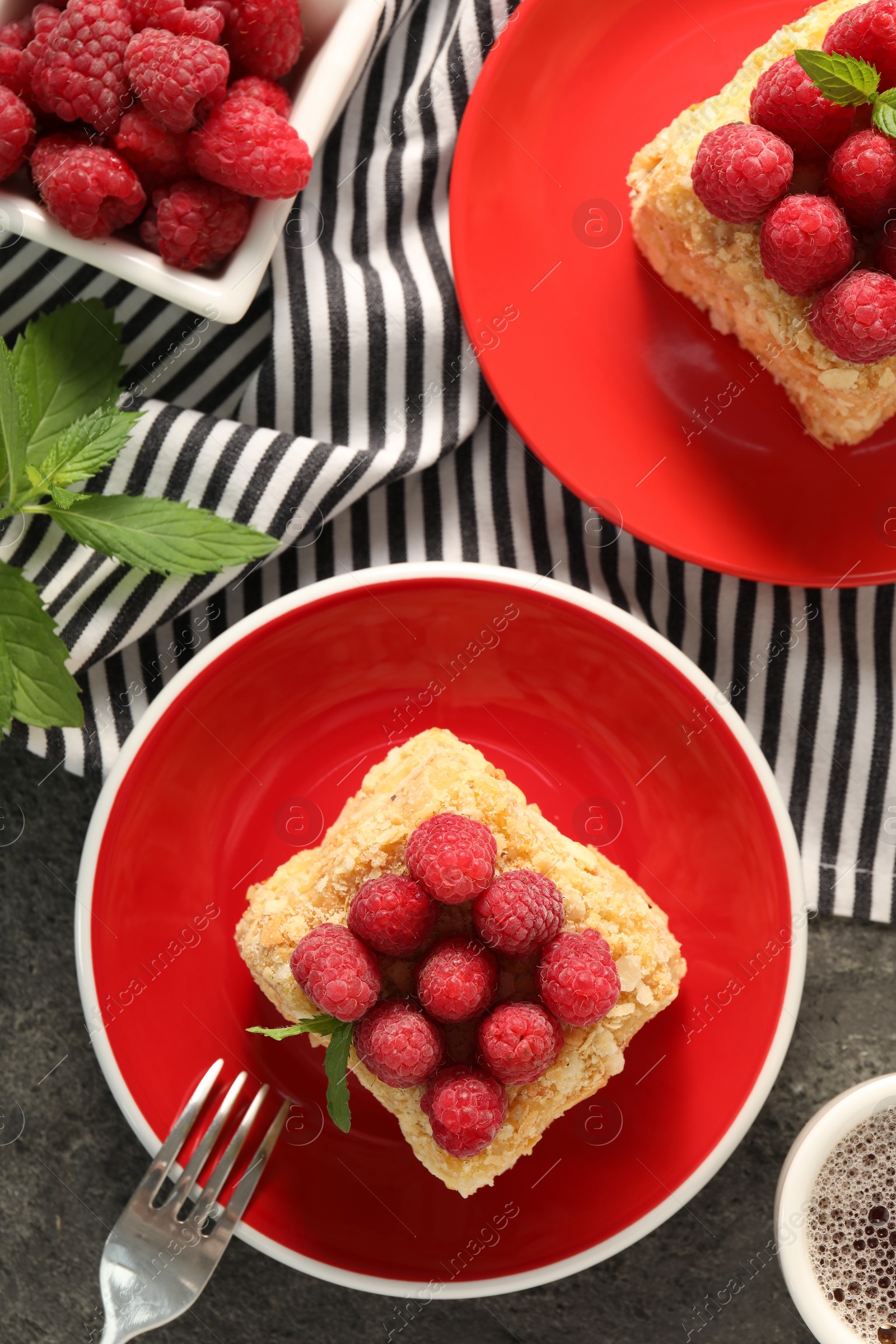 Photo of Pieces of delicious Napoleon cake with fresh raspberries served on grey table, flat lay