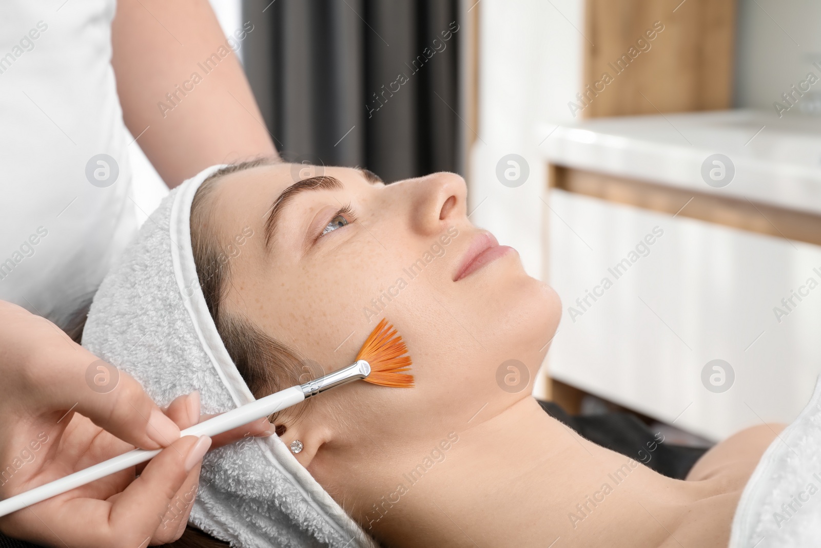 Photo of Cosmetologist with brush applying cosmetic product to client`s face in clinic, closeup