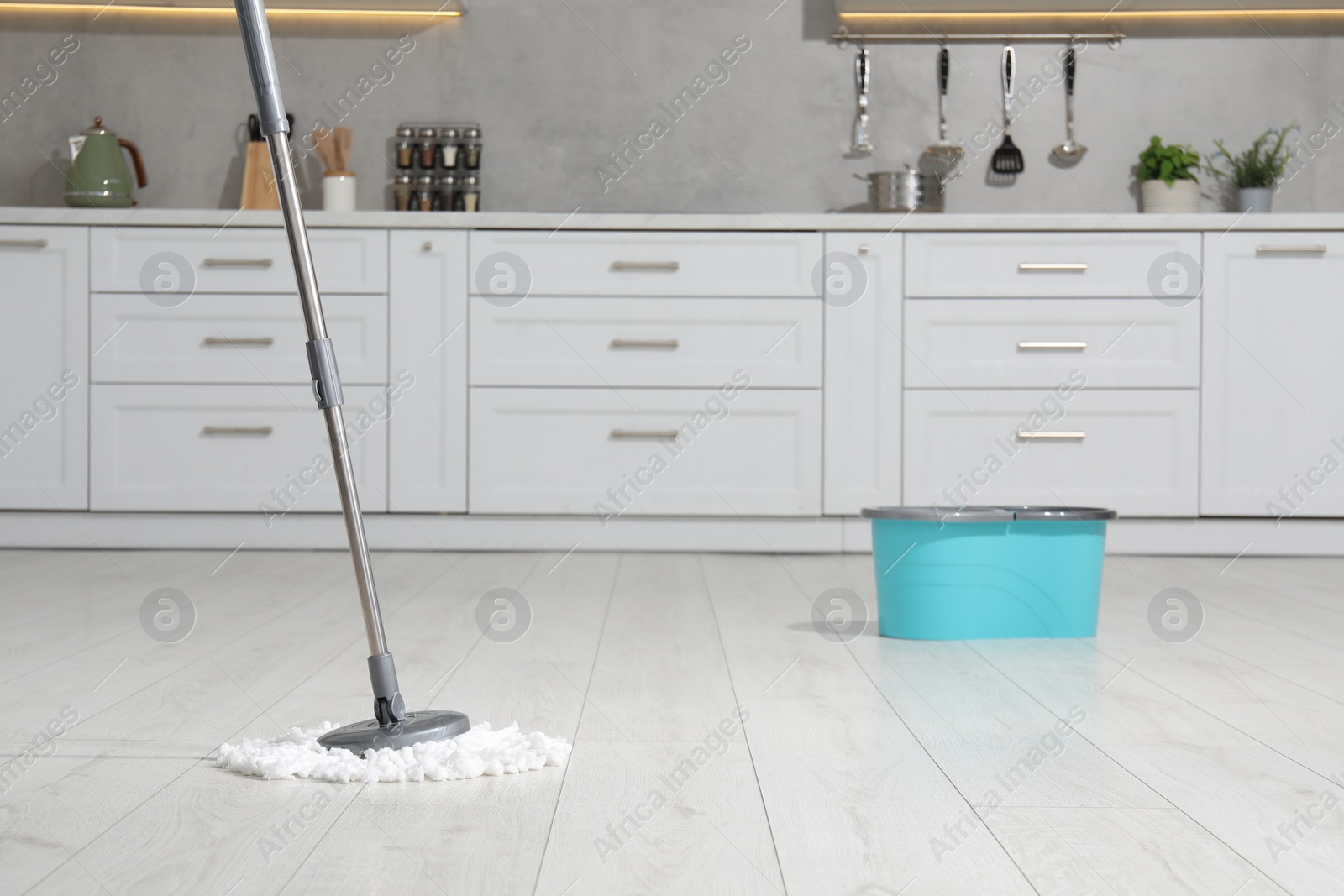 Photo of Mop and bucket on white parquet in kitchen. Cleaning floor