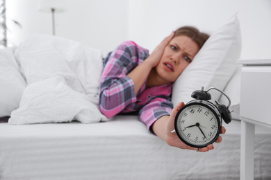 Photo of Emotional young woman with alarm clock at home in morning, focus on hand