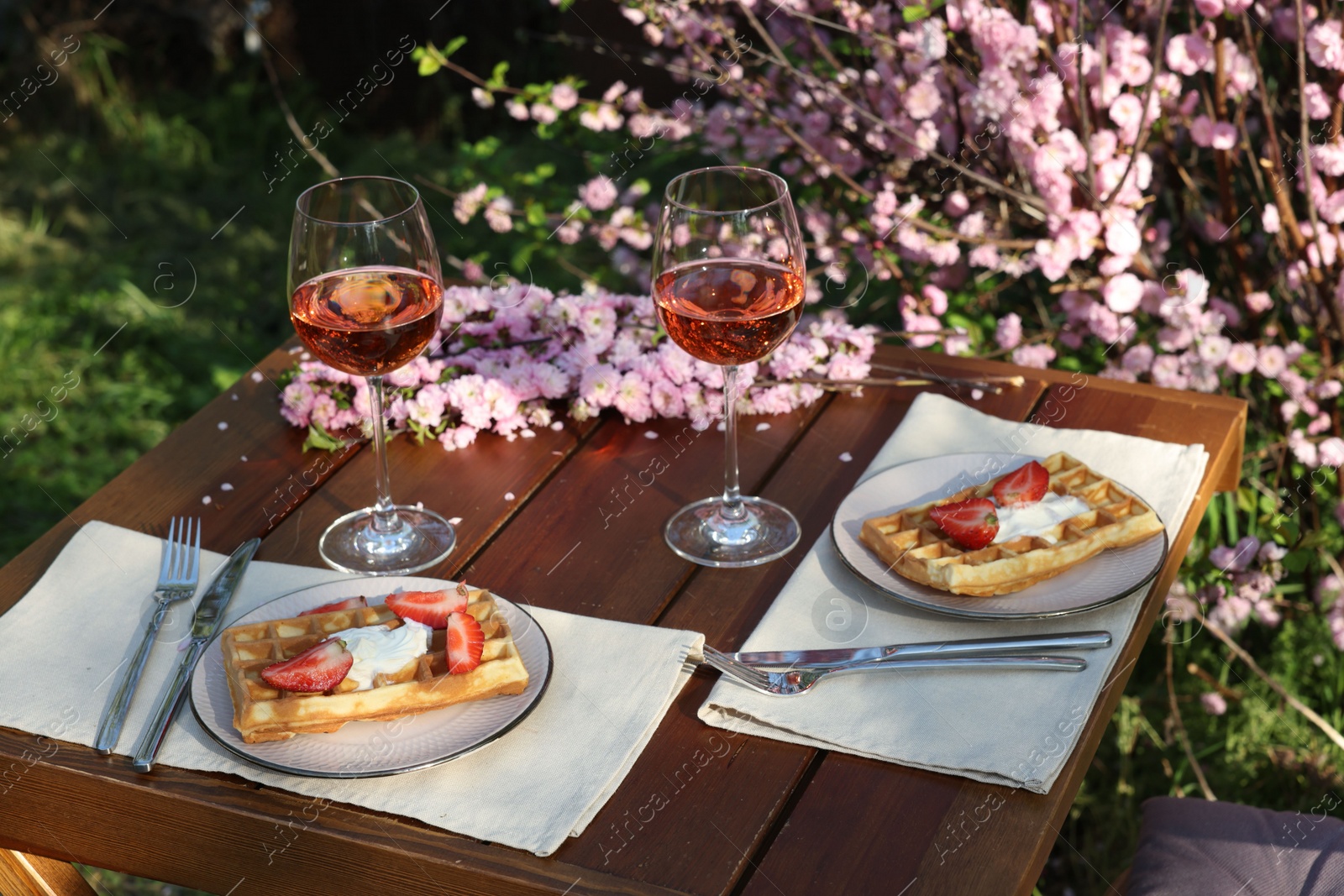 Photo of Delicious Belgian waffles with fresh strawberries and wine served on table in spring garden