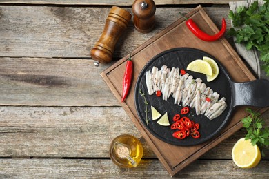 Tasty anchovies with spices and products on wooden table, flat lay. Space for text