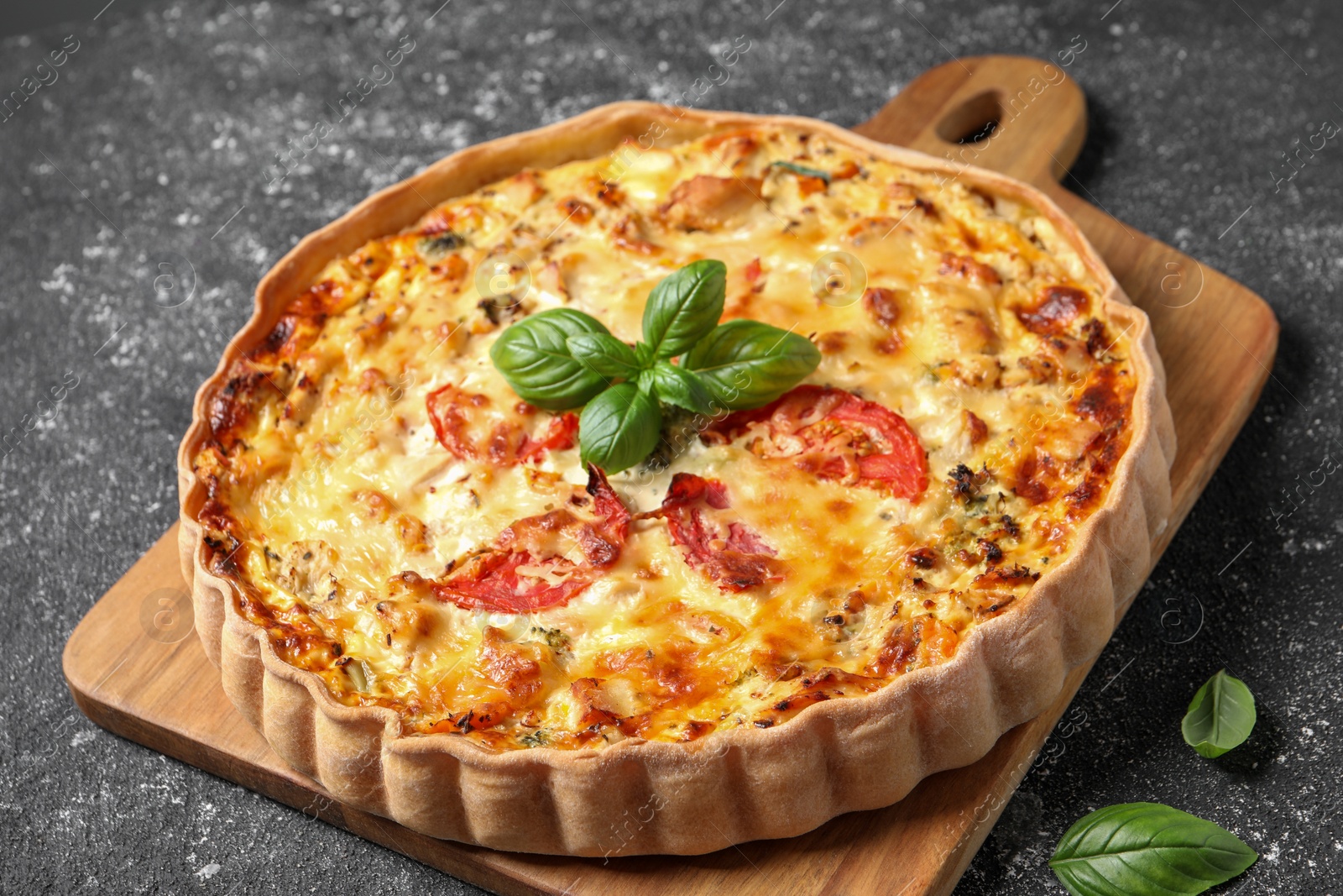 Photo of Tasty quiche with tomatoes, basil and cheese on dark textured table, closeup