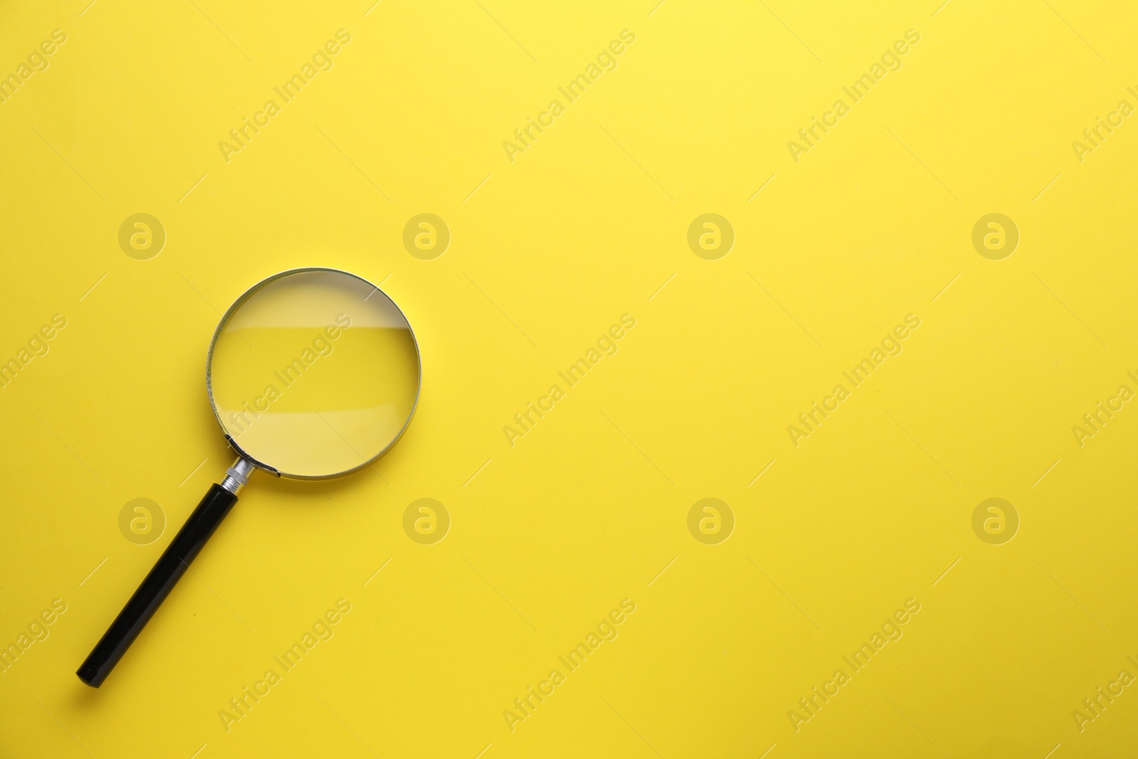 Photo of Magnifying glass on yellow background, top view. Space for text