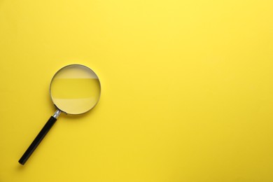 Photo of Magnifying glass on yellow background, top view. Space for text