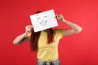 Photo of Woman hiding behind sheet of paper with happy face on red background