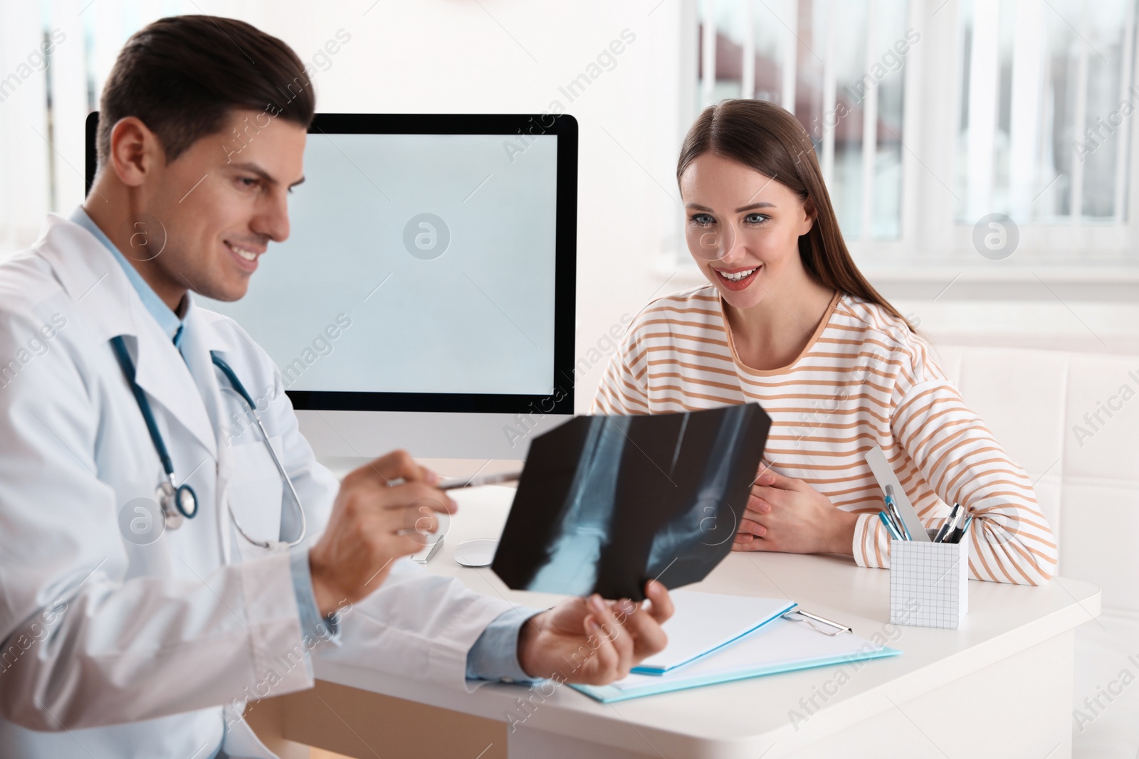 Photo of Orthopedist showing X-ray picture to patient at table in clinic