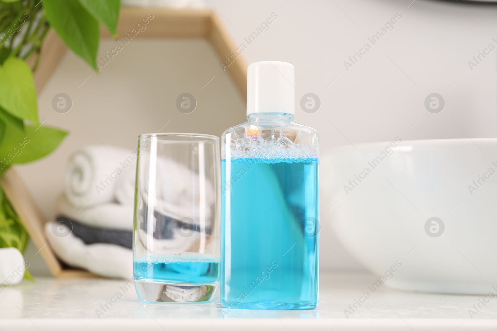 Photo of Bottle of mouthwash and glass on white table in bathroom