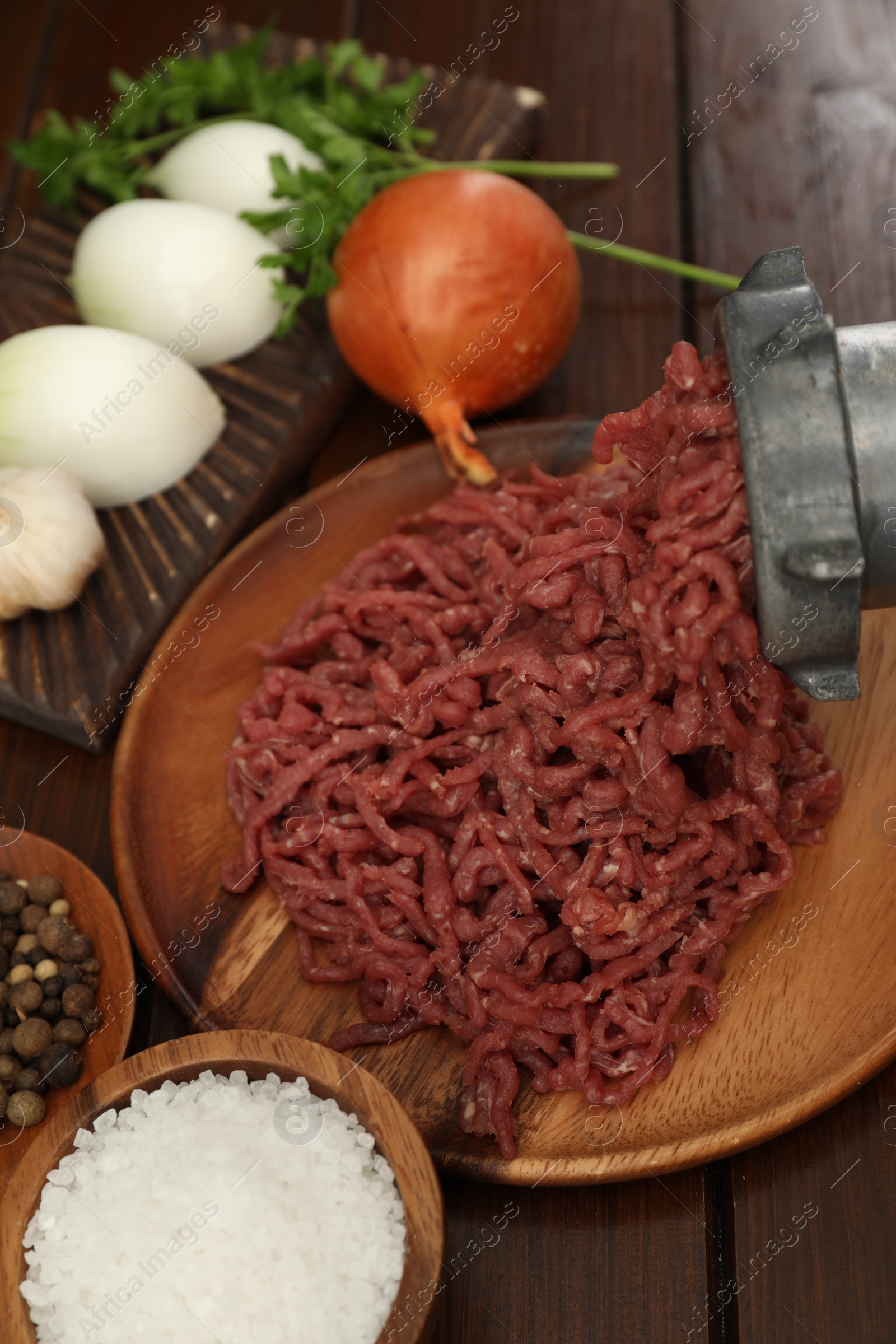 Photo of Meat grinder with beef mince, onion, parsley and spices on wooden table