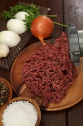 Photo of Meat grinder with beef mince, onion, parsley and spices on wooden table