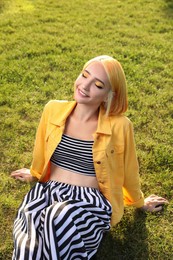 Beautiful young woman with bright dyed hair on green grass