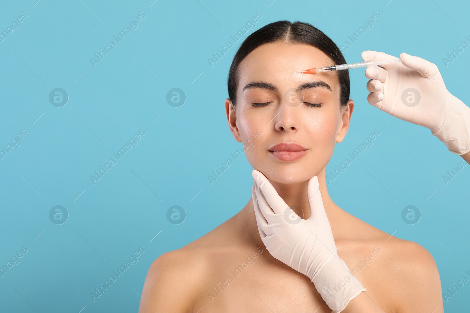 Photo of Doctor giving facial injection to young woman on light blue background, space for text. Cosmetic surgery