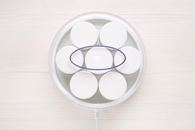 Modern yogurt maker with jars on white wooden table, top view