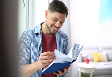 Handsome cheerful man reading book at home