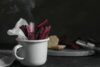 Photo of Tasty cut black carrot in cup on black slate table