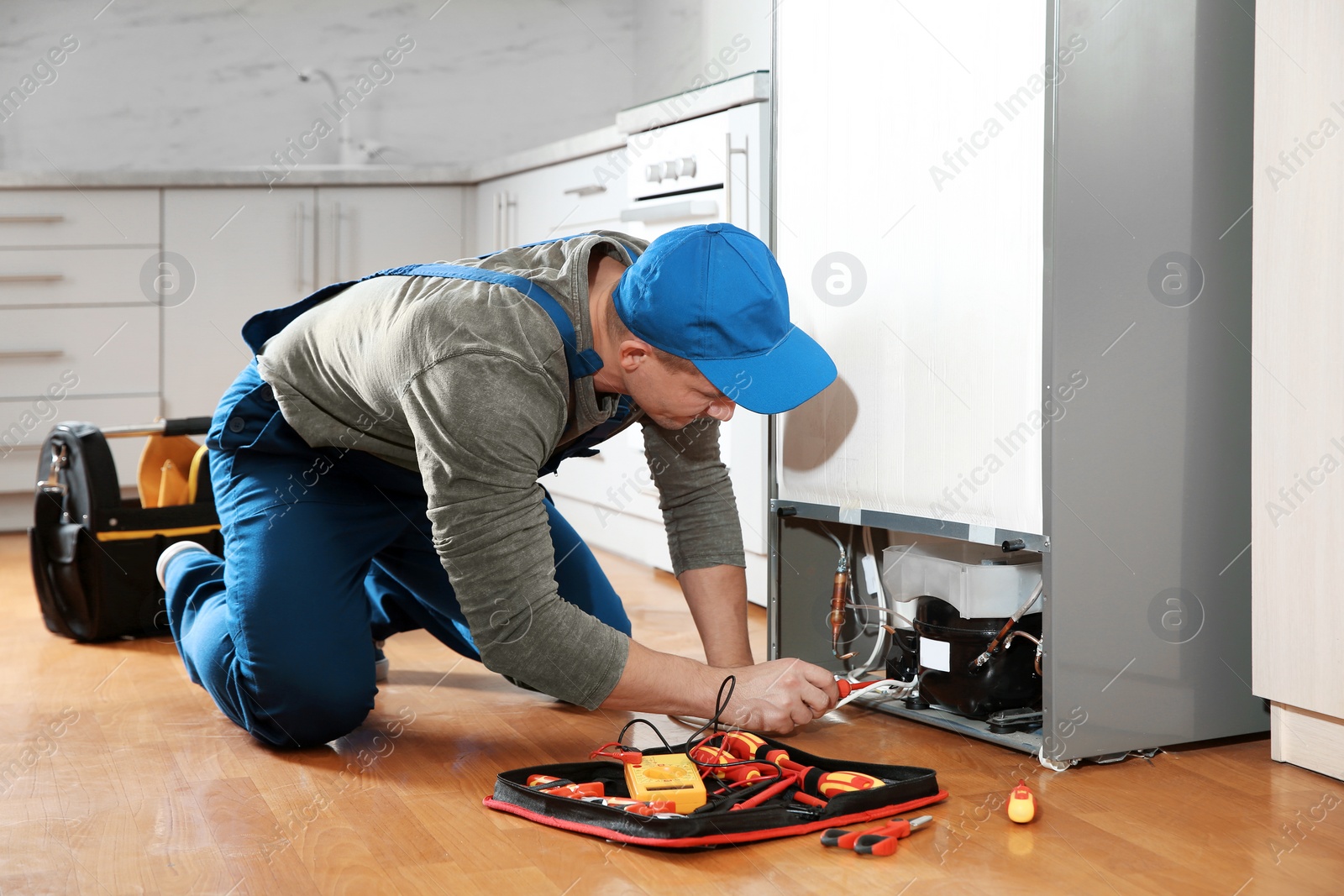 Photo of Male technician in uniform repairing refrigerator indoors