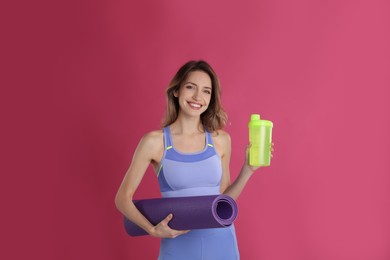 Beautiful woman with yoga mat and shaker on pink background