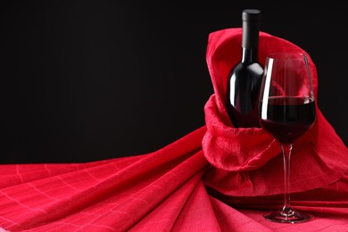 Photo of Stylish presentation of delicious red wine in bottle and glass on black background. Space for text