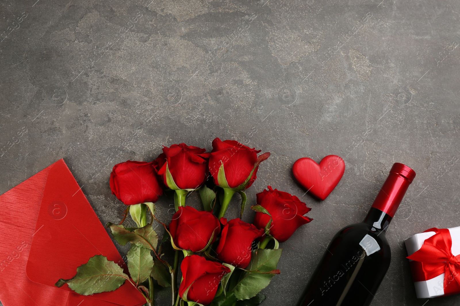 Photo of Flat lay composition with beautiful red roses and bottle of wine on grey background, space for text. Valentine's Day celebration