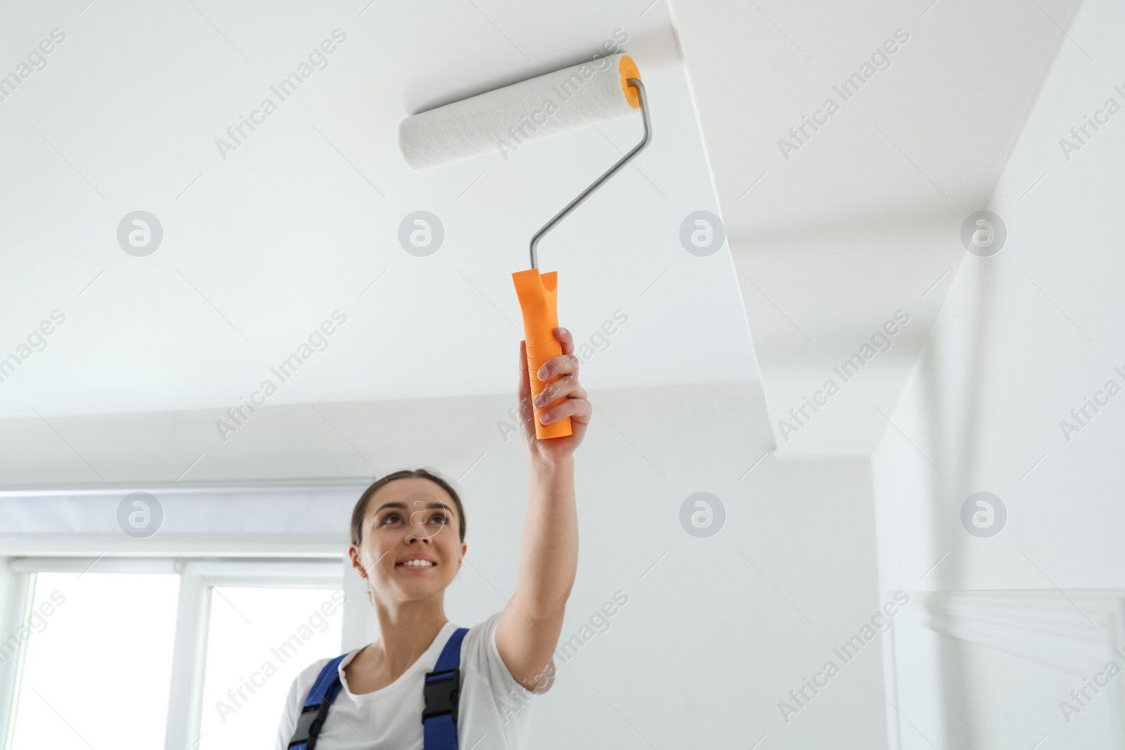 Photo of Worker painting ceiling with white dye indoors