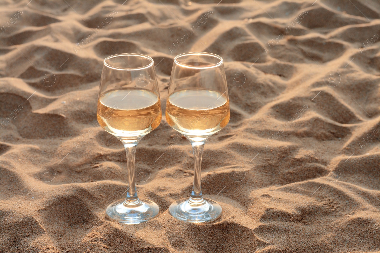 Photo of Glasses of tasty wine on sand, space for text