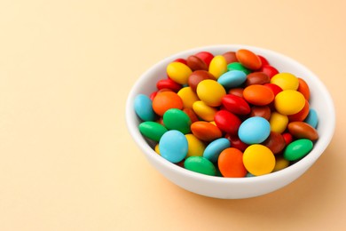 Bowl with tasty colorful candies on beige background, closeup. Space for text