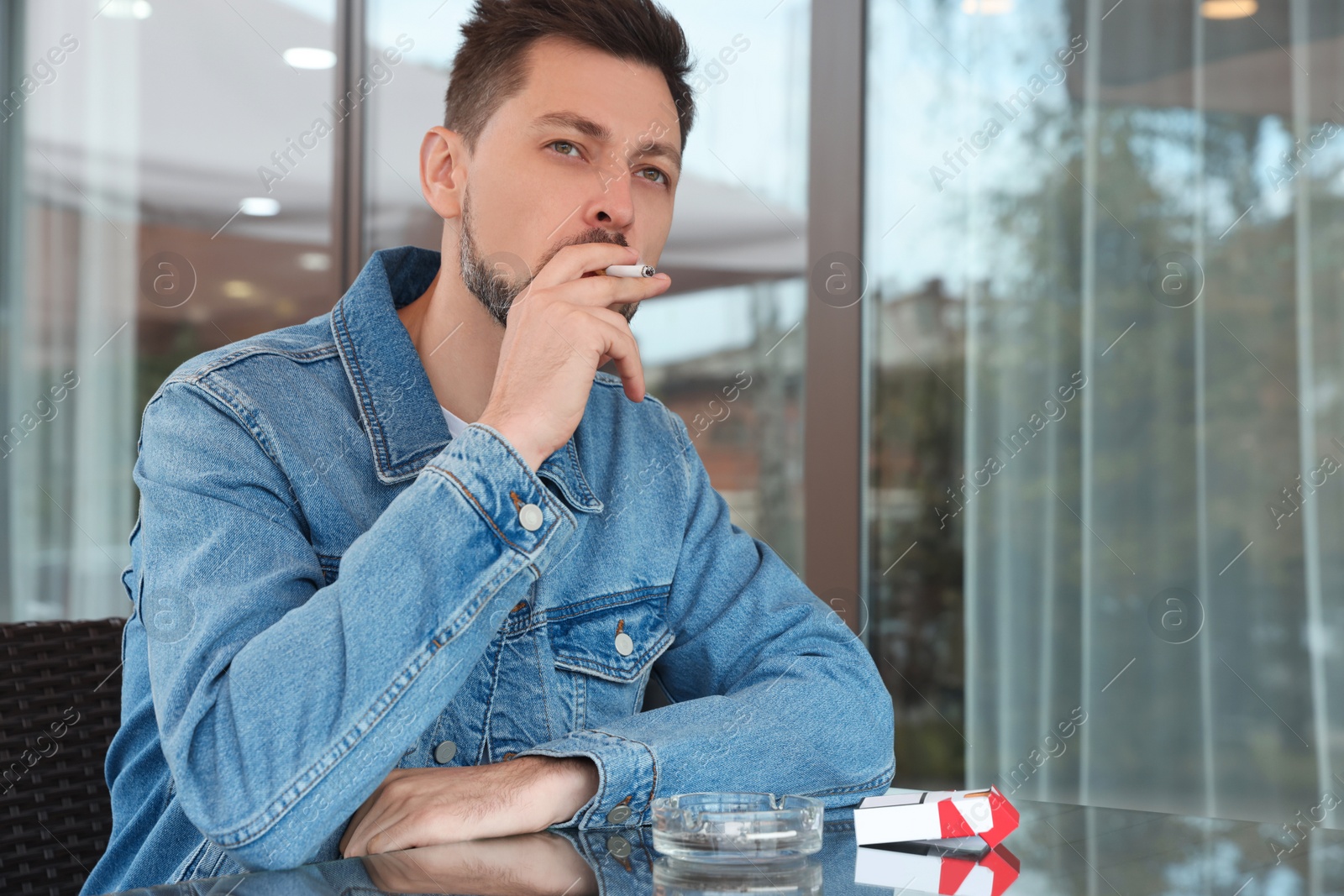 Photo of Handsome man smoking cigarette at table in outdoor cafe